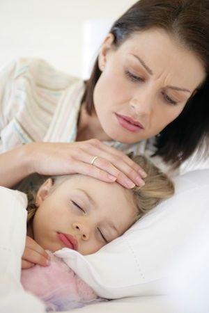 Concerned mother with hand on daughter’s forehead