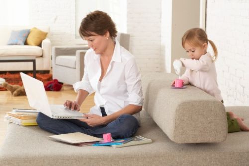 Woman using laptop on sofa by daughter (2-4) pouring drink