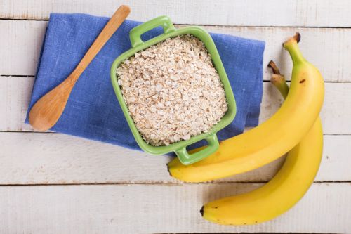 Oat flakes in bowl with bananas  on wooden table. Selective focus.